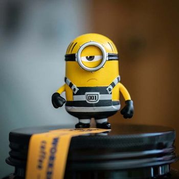 A yellow minion miniature standing atop a black bottle cap.